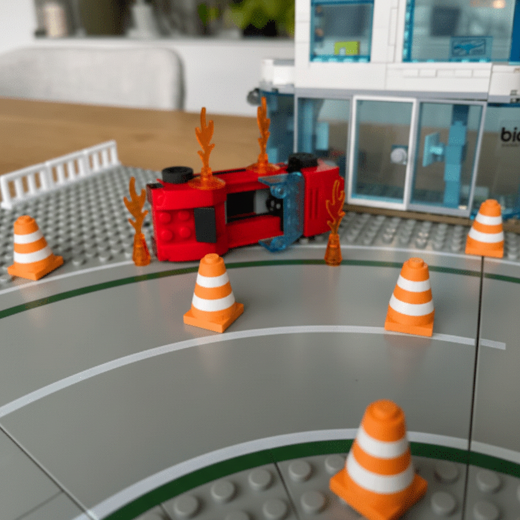 Toy fire truck on a playset with traffic cones and a building in the background