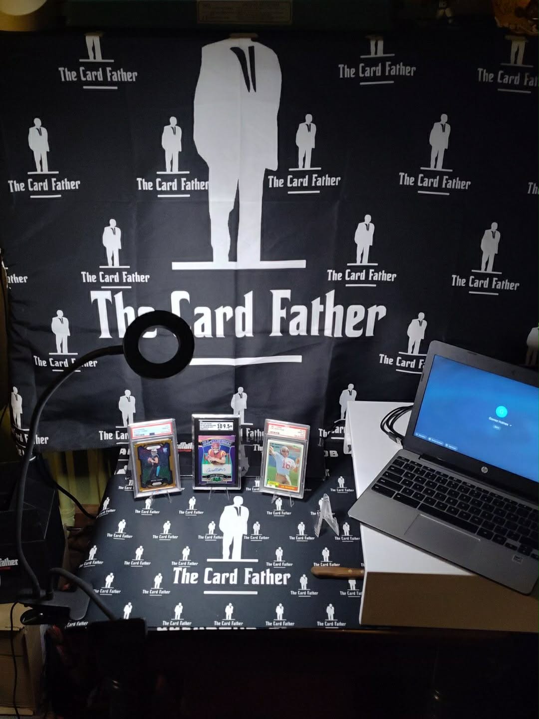 Table with 'The Card Father' branded backdrop, cards, and a laptop.