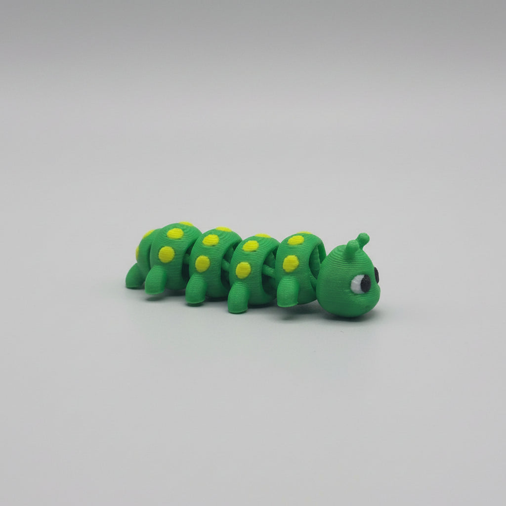 Green caterpillar toy with yellow spots on a brown branch against a textured silver background