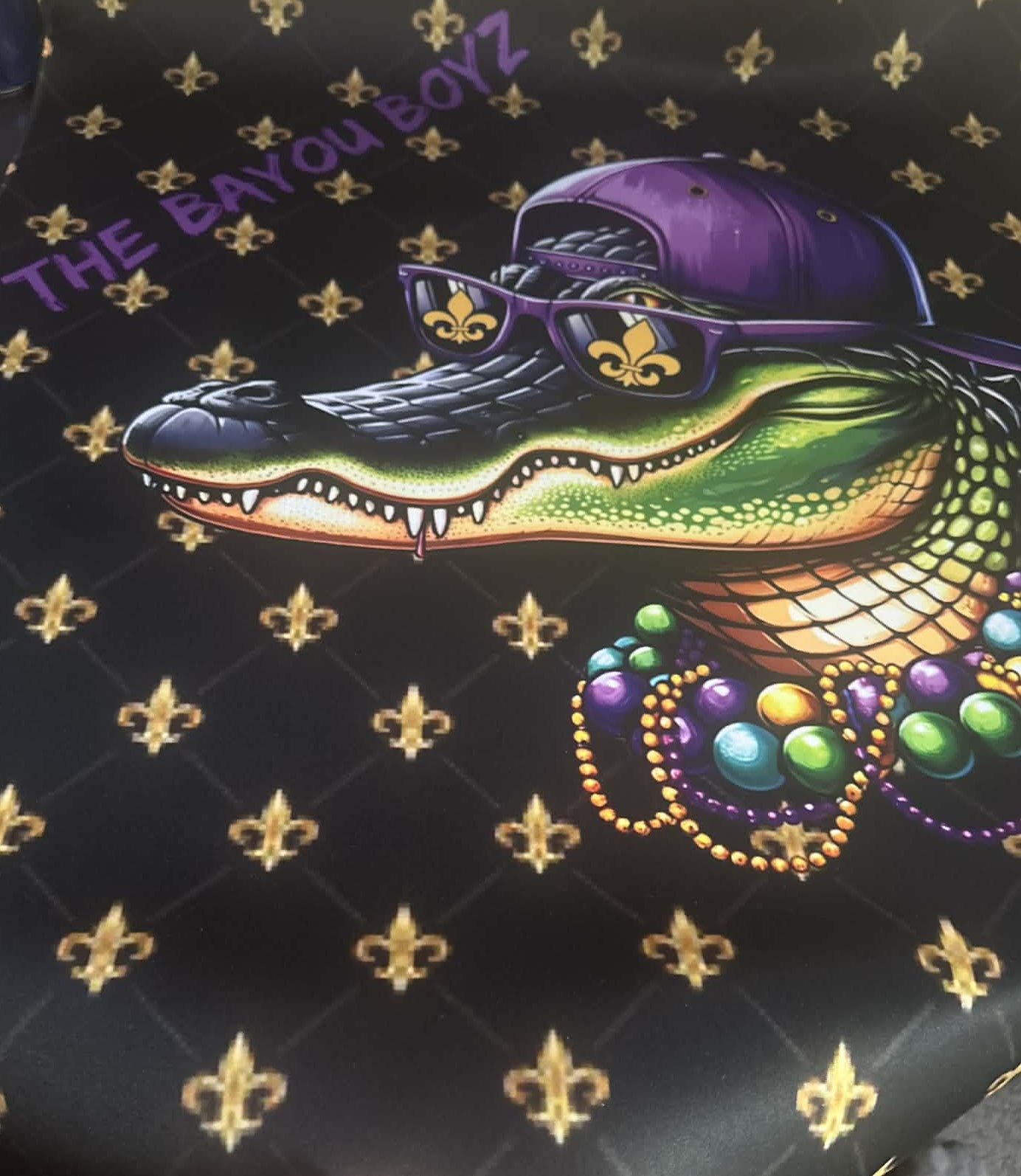 Colorful alligator design with sunglasses and beads on a black background with gold fleur-de-lis patterns, featuring 'The Bayou Boyz' text.