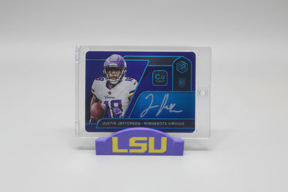 Football trading card of a player from LSU on a marble surface with sports memorabilia in the background.