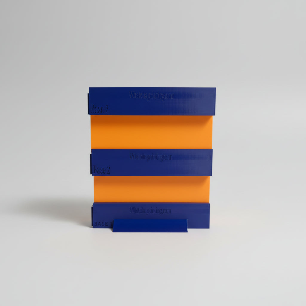 Stack of blue and orange 3D-printed blocks with 'Whatchaprinting.com' branding on a dark surface.
