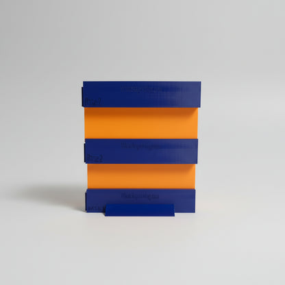 Stack of blue and orange 3D-printed blocks with 'Whatchaprinting.com' branding on a dark surface.