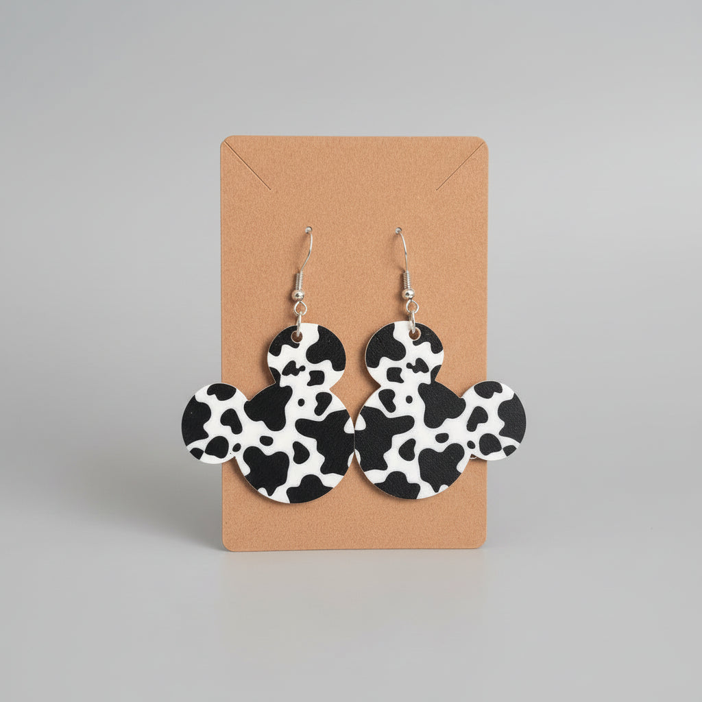 Cow print earrings on a cardboard backing against a dark background