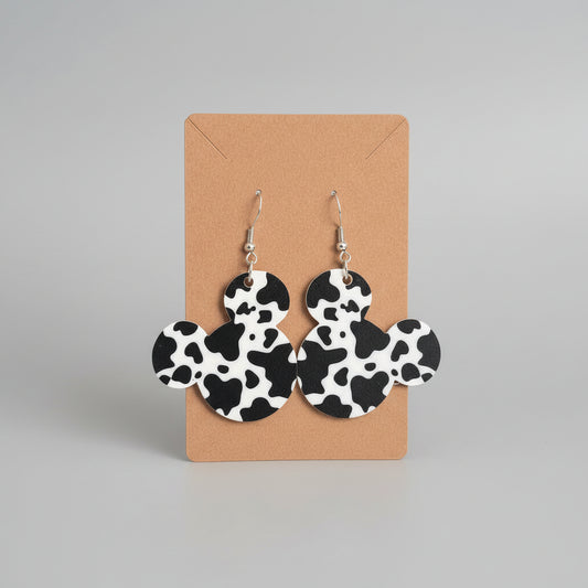 Cow print earrings on a cardboard backing against a dark background