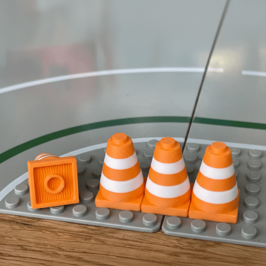 Three orange traffic cone toys on a gray LEGO baseplate with a clear background.