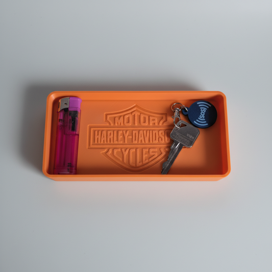 Orange Harley-Davidson tray with keys and a vape pen on a wooden surface with a logo in the background.