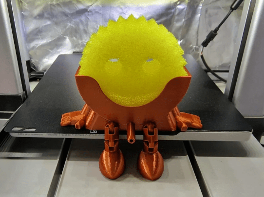 3D-printed orange and yellow creature on a 3D printer bed
