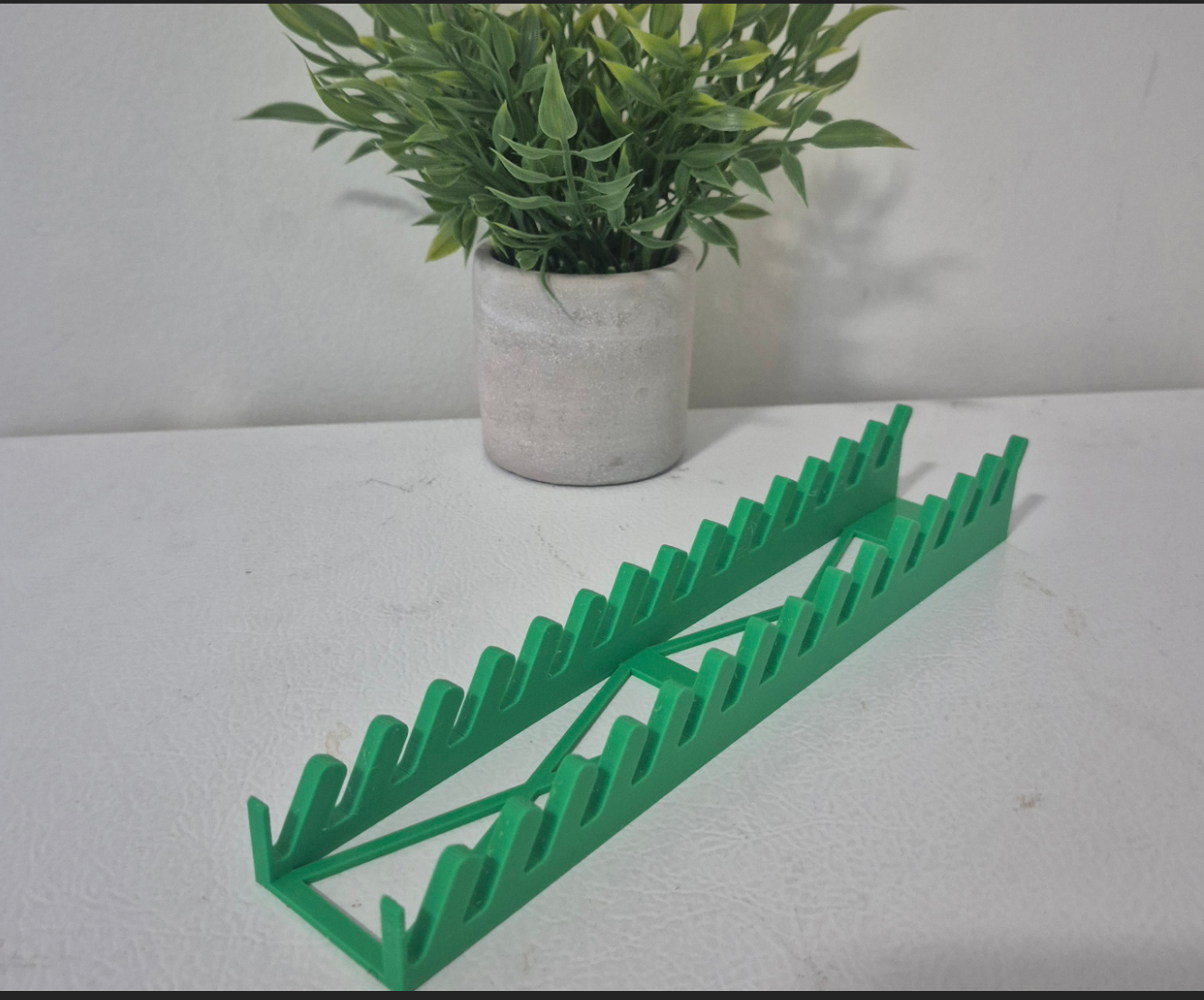 Green plastic plant stand on a white surface with a potted plant in the background
