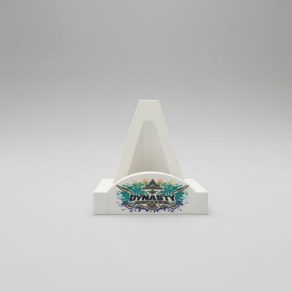 Hand holding a small white cone-shaped object with 'Dynasty' branding against a colorful patterned background.