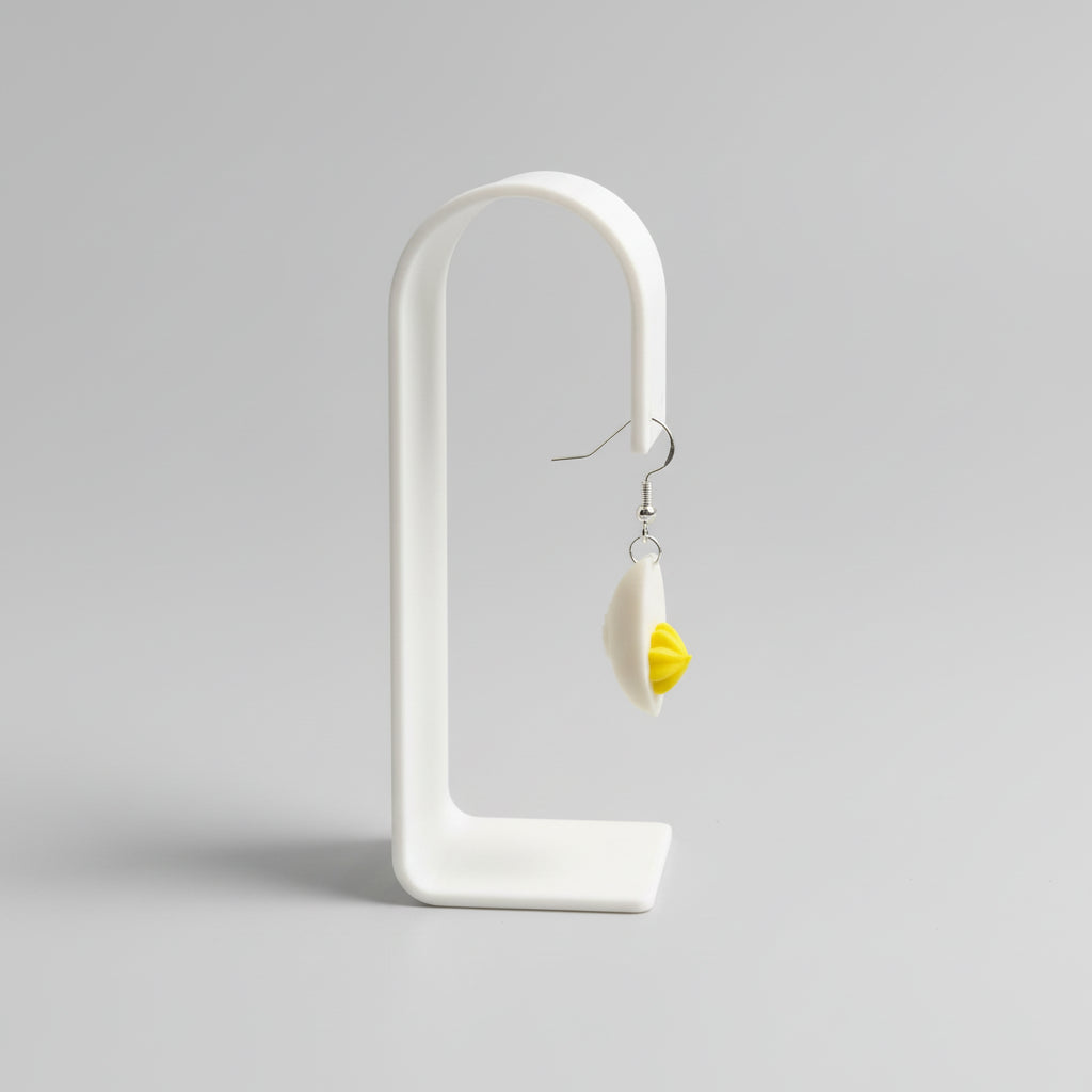 Yellow flower-shaped earring on a white stand with floral wallpaper background