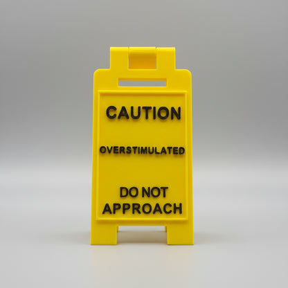 Yellow sign with text 'CAUTION OVERSTIMULATED DO NOT APPROACH' on a textured background