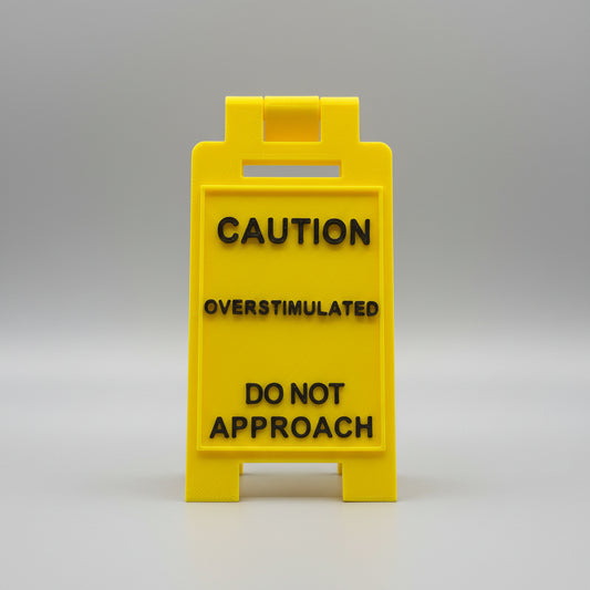 Yellow sign with text 'CAUTION OVERSTIMULATED DO NOT APPROACH' on a textured background