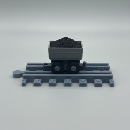 Toy train track with a cart full of coal on a reflective surface