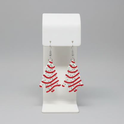 Christmas tree-shaped earrings on a white stand with a floral background