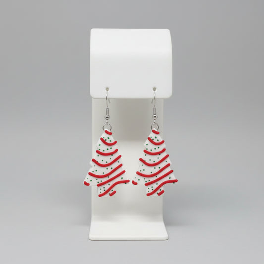 Christmas tree-shaped earrings on a white stand with a floral background