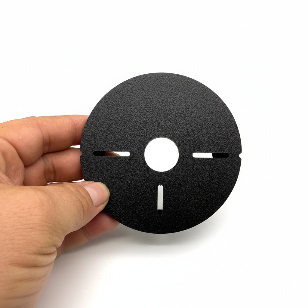 Black circular object with cutouts held by a hand against a textured silver background